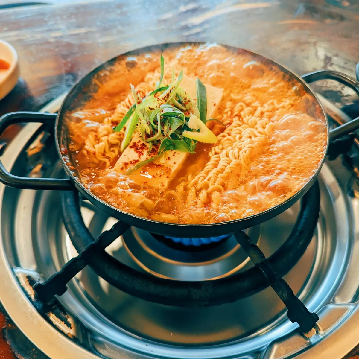 Olla de estofado rojo con fideos y tofu hirviendo en la estufa