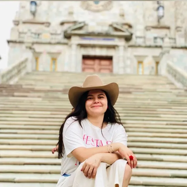 Ivonne, fundadora de Ottoke, sonríe sentada en unas escaleras de piedra con sombrero.